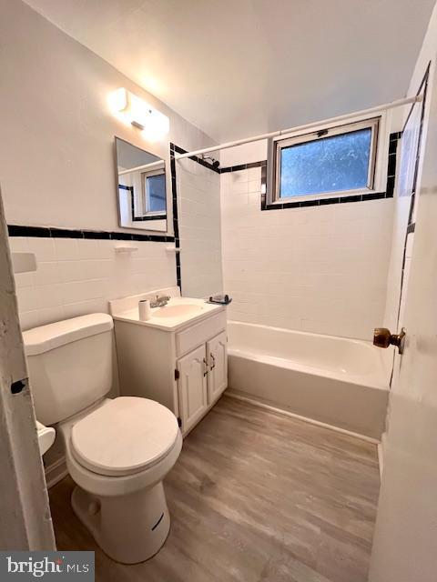 full bathroom featuring vanity, tiled shower / bath combo, tile walls, hardwood / wood-style floors, and toilet