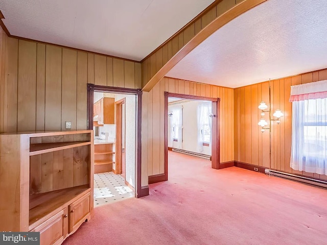 interior space featuring carpet flooring, wood walls, a textured ceiling, and a baseboard heating unit