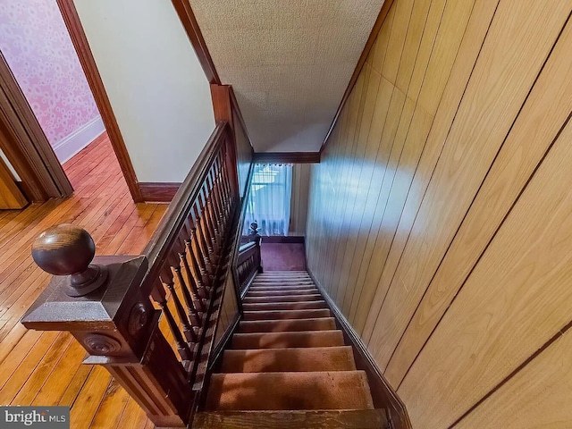 stairway with wood walls, crown molding, and a textured ceiling