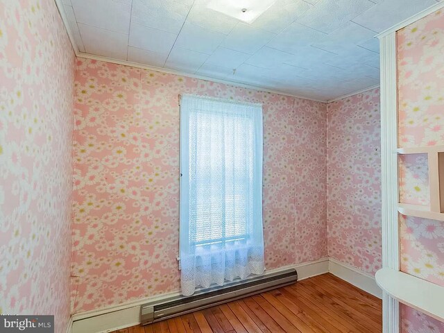 unfurnished room with hardwood / wood-style flooring, ornamental molding, and a baseboard heating unit