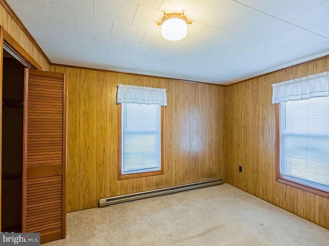 unfurnished room with wooden walls, light colored carpet, and a baseboard heating unit