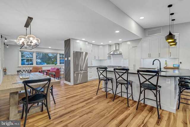 kitchen with white cabinetry, sink, wall chimney range hood, decorative light fixtures, and high end fridge