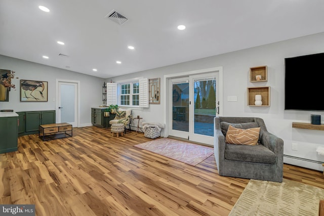 living area with light hardwood / wood-style flooring, vaulted ceiling, and a baseboard heating unit