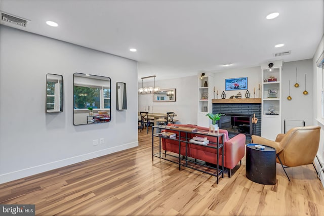 living room featuring an inviting chandelier, light hardwood / wood-style floors, and a brick fireplace