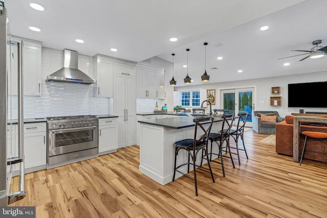 kitchen featuring decorative light fixtures, white cabinetry, wall chimney range hood, and stainless steel stove