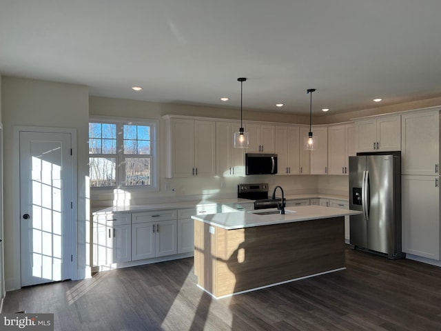 kitchen with hanging light fixtures, appliances with stainless steel finishes, a center island with sink, and white cabinets