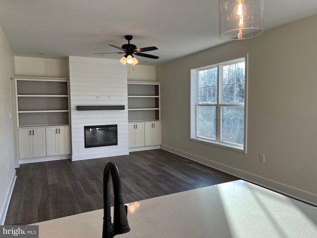 unfurnished living room with dark hardwood / wood-style flooring, a large fireplace, and ceiling fan