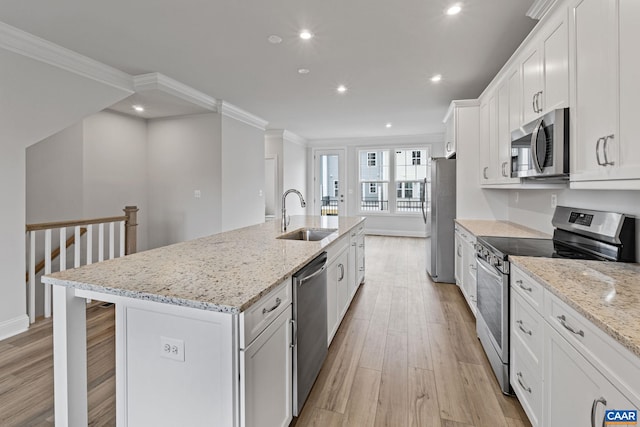 kitchen with light stone counters, stainless steel appliances, sink, white cabinets, and an island with sink