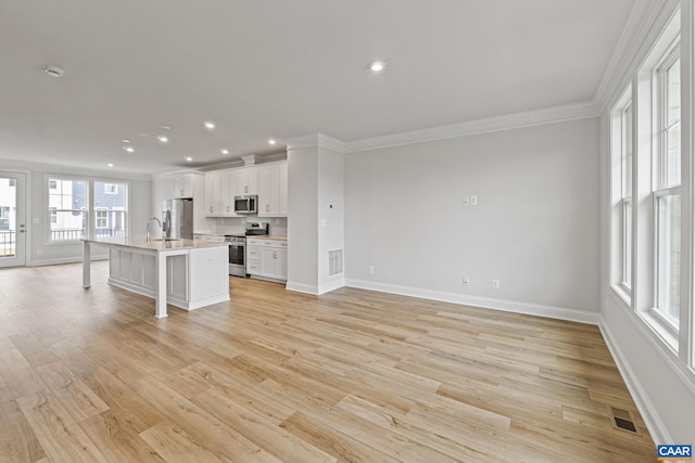 kitchen featuring appliances with stainless steel finishes, an island with sink, a breakfast bar, white cabinets, and light wood-type flooring