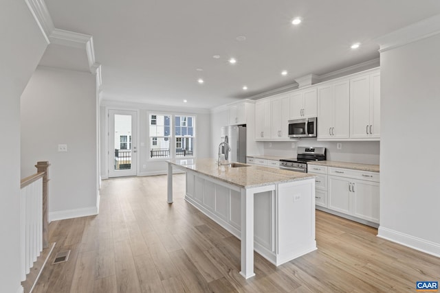 kitchen featuring white cabinets, light stone countertops, stainless steel appliances, and a kitchen island with sink