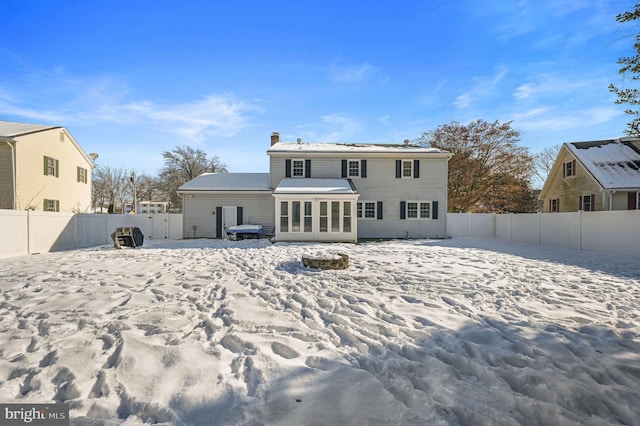 snow covered property featuring a sunroom, a fenced backyard, and a chimney