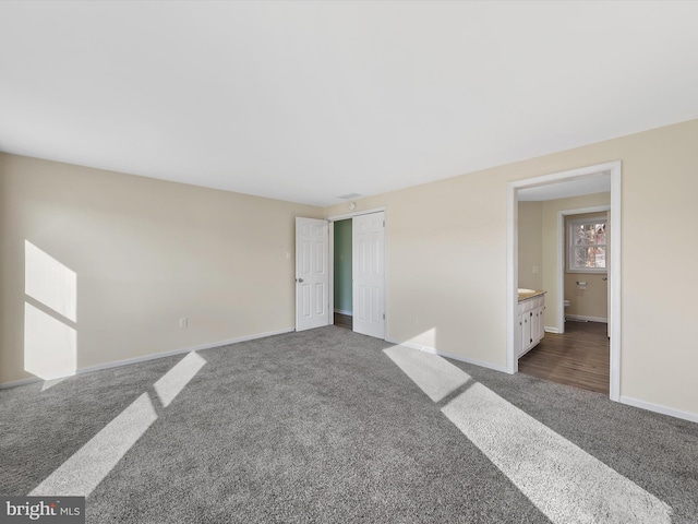 unfurnished bedroom featuring connected bathroom, dark carpet, and a closet