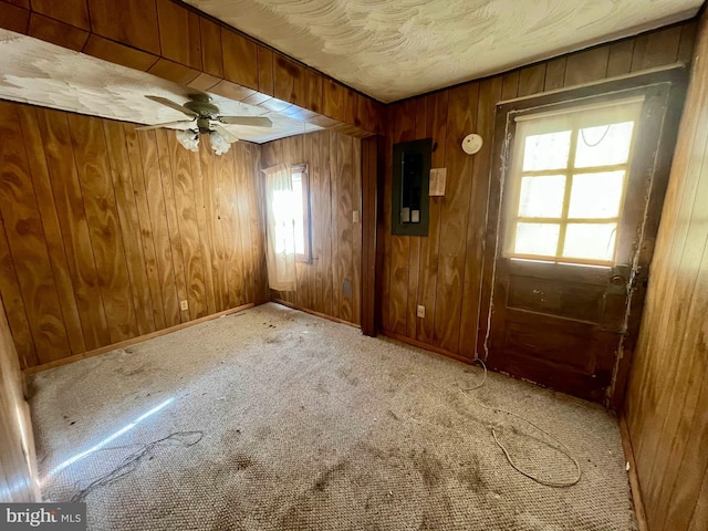 unfurnished room with carpet, ceiling fan, a wealth of natural light, and wood walls