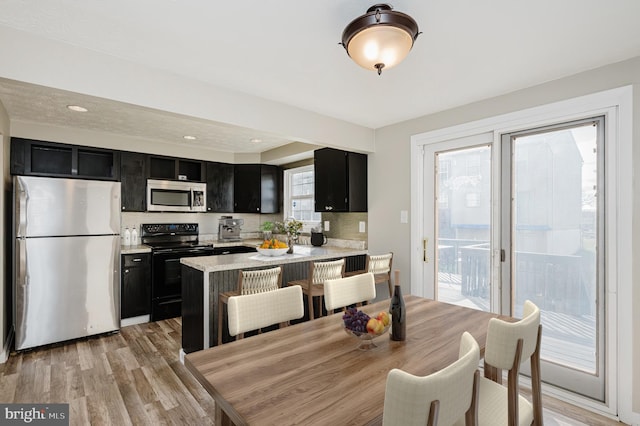 kitchen featuring kitchen peninsula, appliances with stainless steel finishes, a kitchen bar, a wealth of natural light, and light hardwood / wood-style flooring