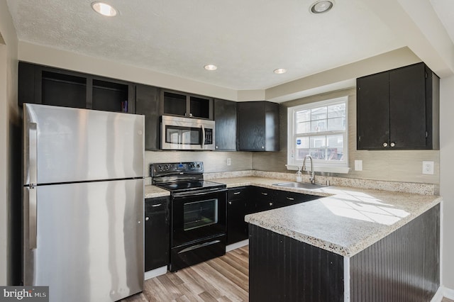 kitchen featuring light stone countertops, sink, kitchen peninsula, appliances with stainless steel finishes, and light wood-type flooring