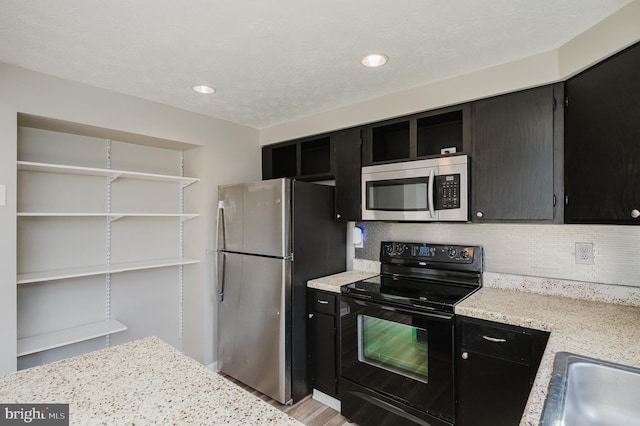 kitchen featuring light stone countertops, stainless steel appliances, tasteful backsplash, light hardwood / wood-style floors, and a textured ceiling