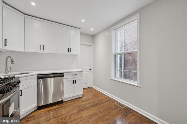 kitchen with sink, dark wood-type flooring, stainless steel appliances, tasteful backsplash, and white cabinets