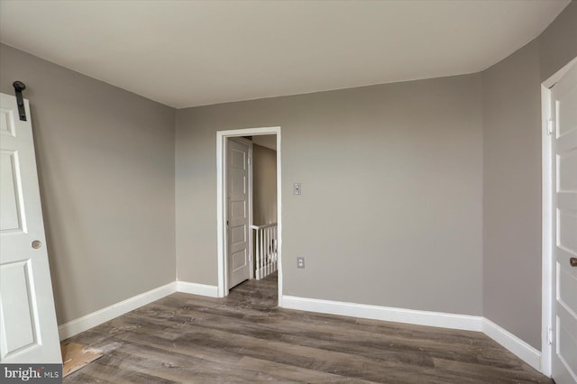 empty room with a barn door and dark wood-type flooring