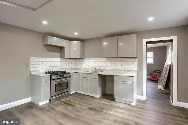 kitchen with tasteful backsplash, gas range, sink, and light hardwood / wood-style floors