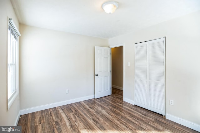 unfurnished bedroom with multiple windows, a closet, and dark wood-type flooring