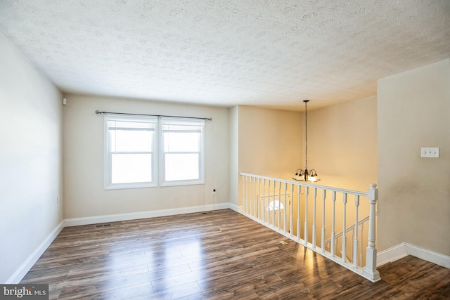 empty room with a chandelier, dark wood-type flooring, and a textured ceiling