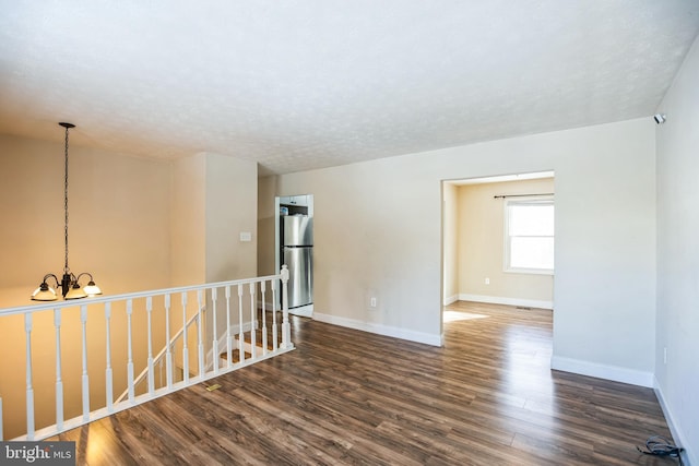 unfurnished room featuring a textured ceiling, dark hardwood / wood-style floors, and an inviting chandelier