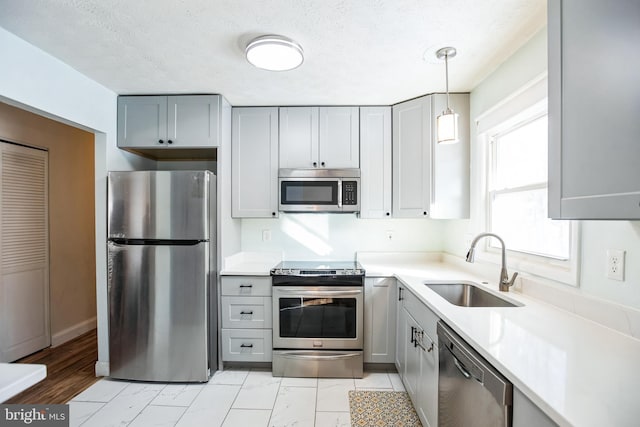 kitchen featuring gray cabinetry, sink, stainless steel appliances, a textured ceiling, and decorative light fixtures