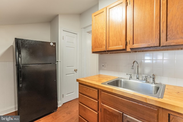 kitchen featuring black fridge, sink, vaulted ceiling, light wood-type flooring, and butcher block counters