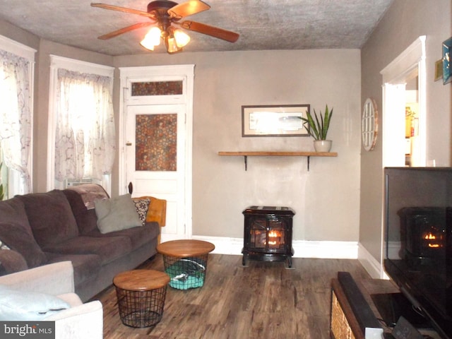 living room featuring ceiling fan, wood-type flooring, and a wood stove