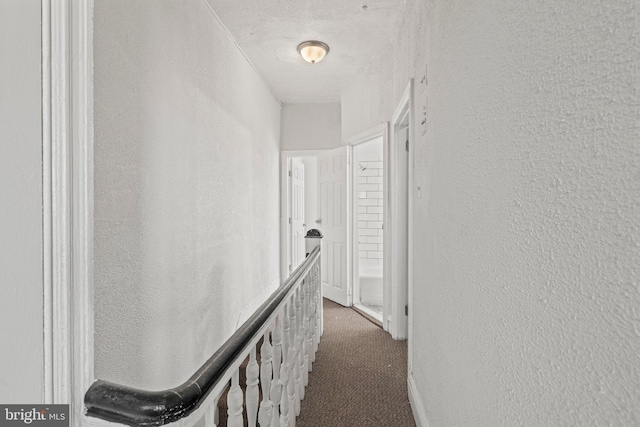 hall featuring a textured ceiling and dark carpet