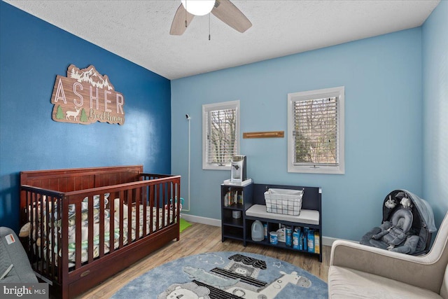 bedroom featuring ceiling fan, wood-type flooring, a crib, and a textured ceiling