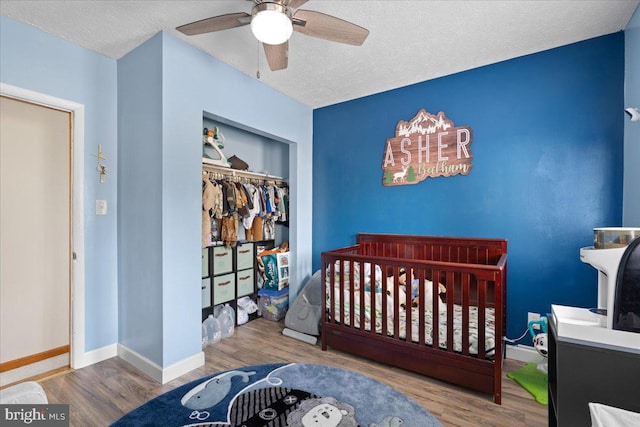 bedroom featuring ceiling fan, hardwood / wood-style floors, a textured ceiling, a closet, and a crib