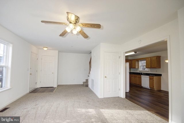 unfurnished living room featuring dark colored carpet, ceiling fan, and sink