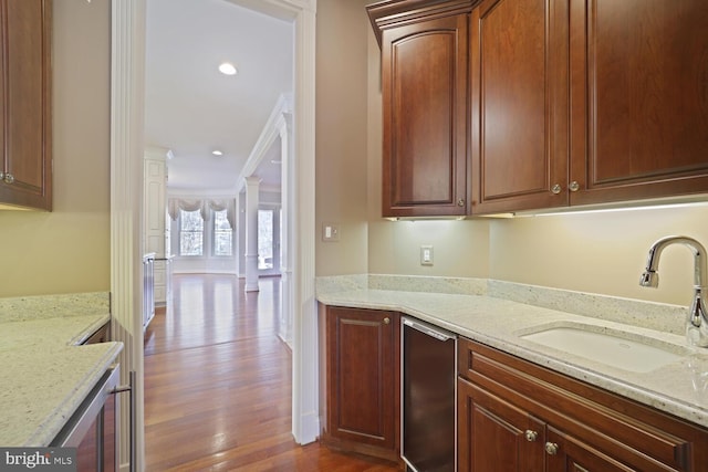 kitchen featuring wine cooler, a sink, light stone countertops, dark wood finished floors, and decorative columns