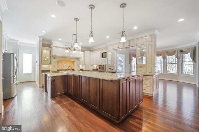 kitchen featuring a spacious island, ornamental molding, freestanding refrigerator, glass insert cabinets, and pendant lighting