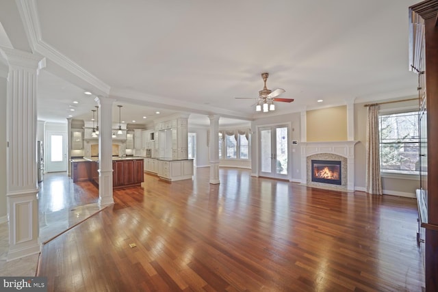 unfurnished living room with wood finished floors, a fireplace with flush hearth, decorative columns, and crown molding