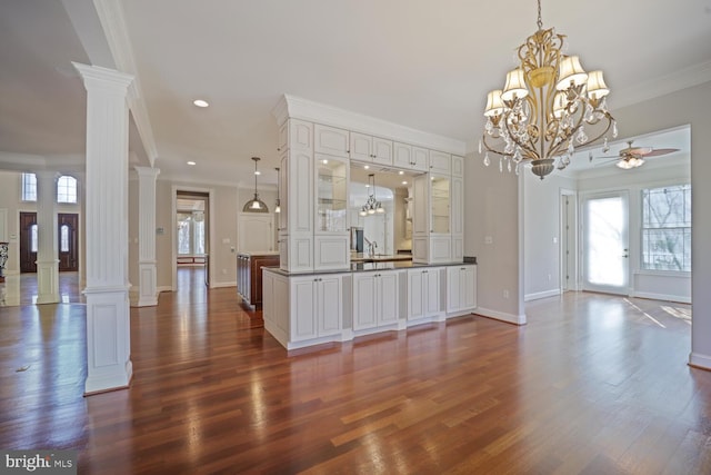 interior space with decorative light fixtures, dark wood finished floors, glass insert cabinets, white cabinetry, and ornate columns