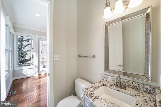 half bathroom with toilet, ornamental molding, vanity, wood finished floors, and baseboards