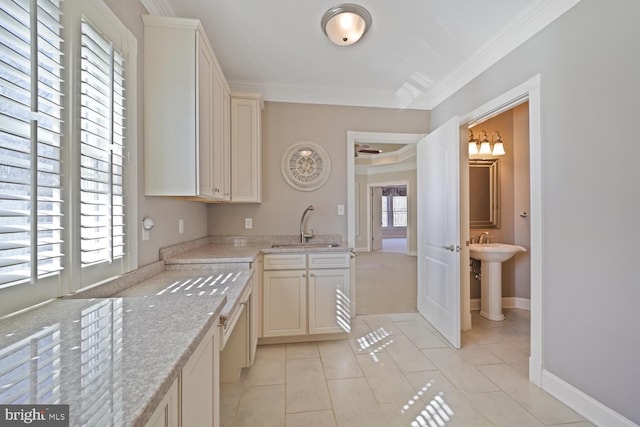 kitchen with light tile patterned floors, ornamental molding, a sink, and light stone counters