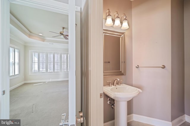 bathroom with a tray ceiling, crown molding, a sink, ceiling fan, and baseboards