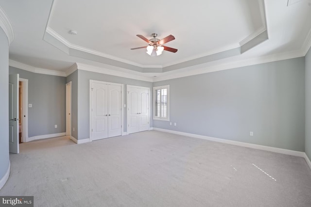 unfurnished bedroom featuring light carpet, baseboards, multiple closets, a raised ceiling, and crown molding