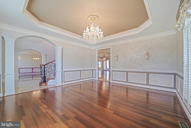 spare room featuring a decorative wall, wood finished floors, visible vents, a tray ceiling, and decorative columns