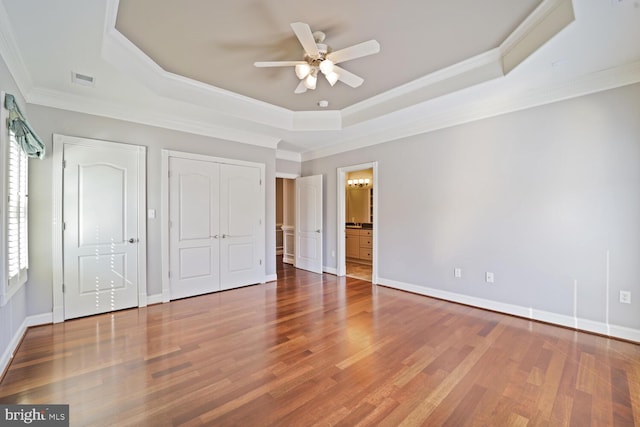 unfurnished bedroom featuring baseboards, a raised ceiling, wood finished floors, and ornamental molding