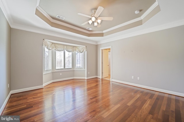 empty room with baseboards, visible vents, a tray ceiling, and wood finished floors