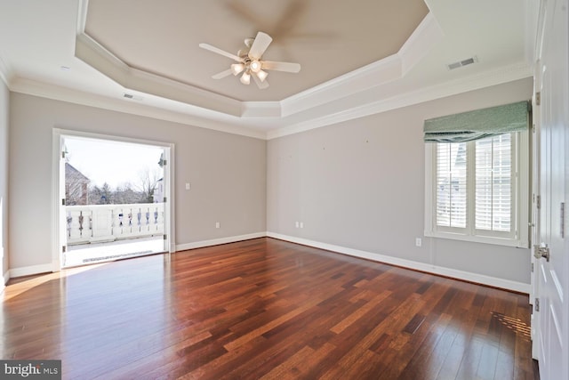 empty room featuring a tray ceiling, dark wood-type flooring, visible vents, and crown molding