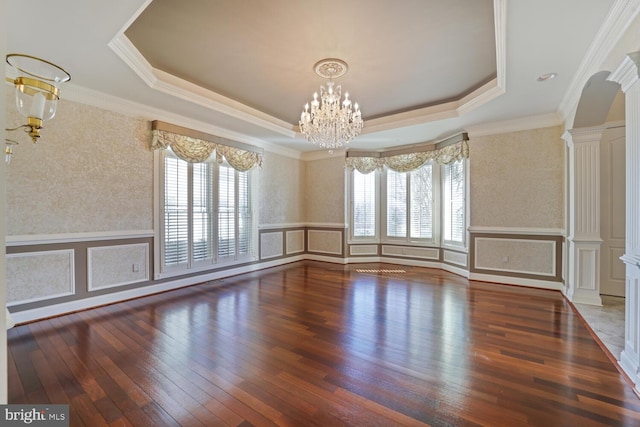 empty room featuring a decorative wall, a tray ceiling, dark wood-type flooring, and ornate columns