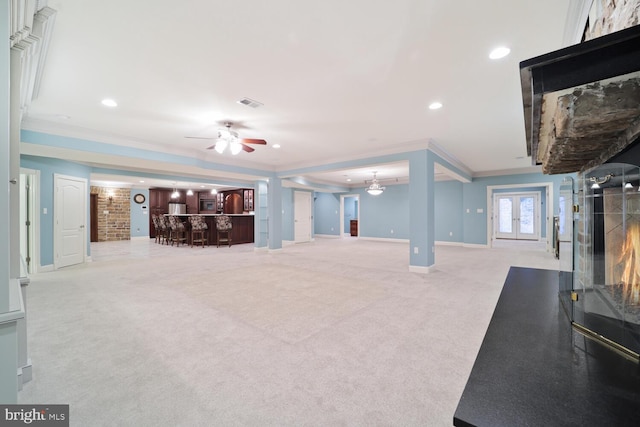 unfurnished living room featuring light carpet, a warm lit fireplace, a dry bar, baseboards, and ornamental molding