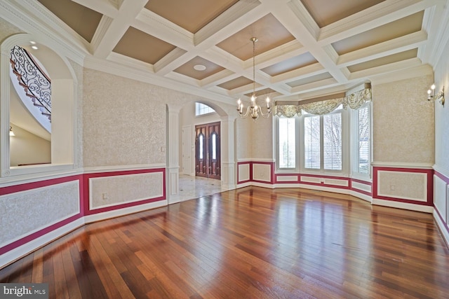 spare room with arched walkways, a notable chandelier, wood finished floors, beamed ceiling, and decorative columns