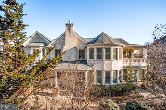 view of front facade with brick siding, a chimney, and a balcony