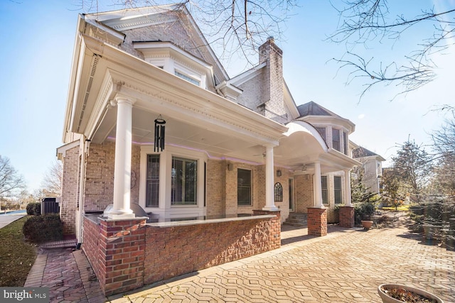 view of property exterior featuring covered porch, brick siding, a chimney, and central air condition unit